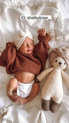 a baby laying on top of a bed next to a teddy bear wearing a knitted hat