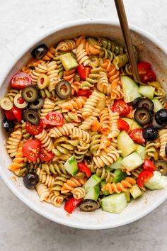 a bowl filled with pasta salad and olives, cucumber, tomato, onion, pickles