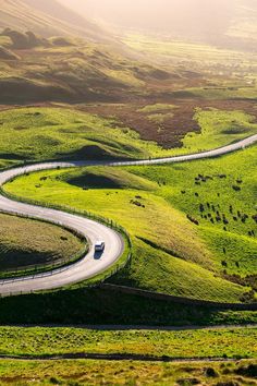 a car driving down a curvy road in the country side with rolling hills