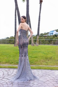 a woman standing in front of some palm trees wearing a dress with feathers on it