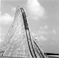 a black and white photo of a large roller coaster at an amusement park with people on it