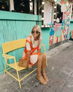 a woman sitting on a yellow bench in front of a colorful building with a blue wall