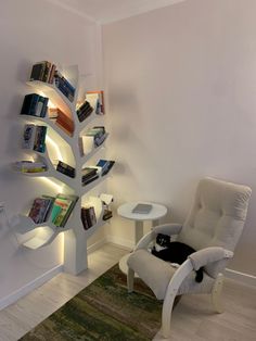 a cat sitting in a chair next to a tree shaped book shelf filled with books