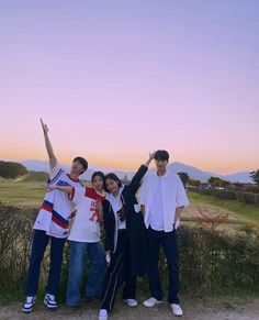 four people standing in front of a fence with their arms up and one person pointing at the sky