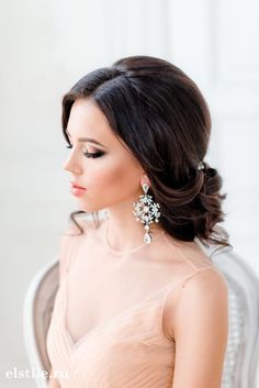 a woman in a dress sitting on a chair with her hair up and wearing earrings