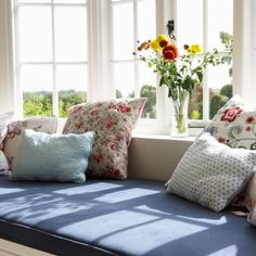 a window seat with pillows on it and flowers in the vase next to each other