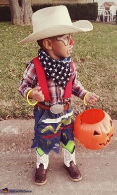 a little boy dressed up as a cowboy holding a jack - o'- lantern