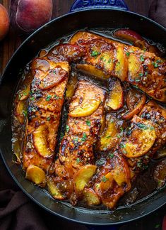 a pan filled with meat and potatoes on top of a table next to peaches