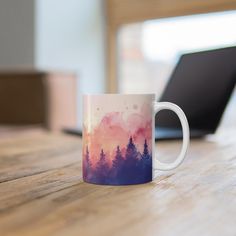 a coffee mug sitting on top of a wooden table next to a laptop computer in the background