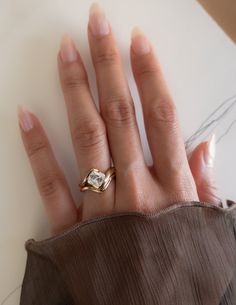 a woman's hand with a gold ring on top of her left hand and a brown shirt underneath it