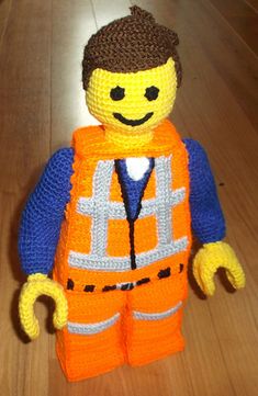 a crocheted construction worker doll sitting on top of a wooden floor in an orange vest