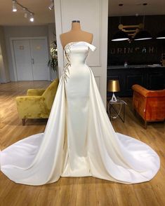 a white wedding dress on display in a room with wooden floors and furniture, including a mannequin