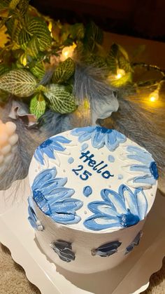 a blue and white cake sitting on top of a table next to some plants with lights in the background