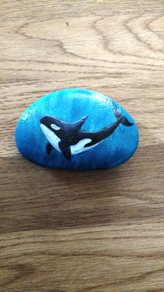 an orca whale painted on a rock sitting on top of a wooden table next to a cell phone