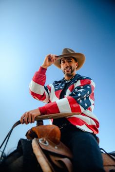 a man sitting on top of a horse wearing a cowboy hat and american flag shirt