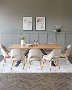 a dining room table with chairs and pictures on the wall above it, in front of a chevron wood floor