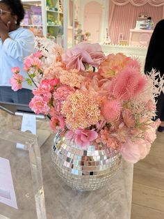 a vase filled with lots of pink flowers on top of a glass table next to a mirror ball