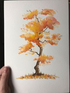 a person holding up a watercolor painting of a tree with orange leaves on it