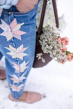 a person wearing blue jeans with flowers on them and holding a handbag in the snow