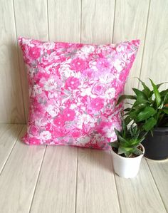 a pink flowered pillow sitting next to a potted plant