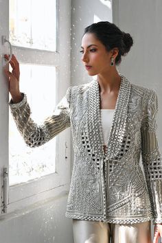 A slate coloured tissue jacket with folded lapels is rendered with intricate cutwork and thread and embroidery. Paired with ivory choli and slate-coloured charmeuse box trousers with embroidered hems; this outfit exudes sheer elegance. Model Height is 5'6 jacket length is 26" Elegant Traditional Drape Outerwear For Party, Elegant Party Outerwear With Traditional Drape, Elegant Silk Nehru Jacket With Chikankari Embroidery, Elegant Formal Outerwear With Chikankari Embroidery, Elegant Silk Sherwani With Resham Embroidery, Elegant Long Sleeve Bandhgala With Resham Embroidery, Elegant Silk Bandhgala With Chikankari Embroidery, Elegant Embellished Sherwani For Festive Occasions, Elegant Festive Embellished Sherwani