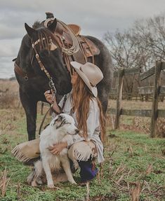 a woman kneeling down next to a horse with a dog and a cowboy hat on