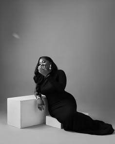 a black and white photo of a woman in a long dress sitting on a box