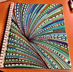 a spiral notebook with colorful lines on it sitting on a table next to a pen