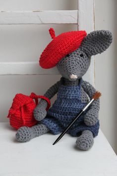 a crocheted gray and red mouse with a paintbrush