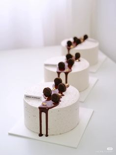 three white cakes with chocolate sauce and toppings on each one side, lined up in rows