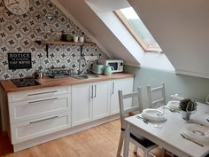 a kitchen with white cabinets and wooden flooring next to an attic style wallpaper