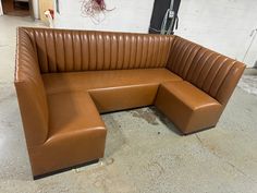 a brown leather couch sitting on top of a cement floor next to a white wall