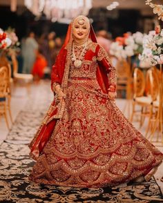 a woman in a red and gold bridal gown standing on a rug with flowers