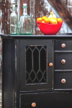 a bowl of fruit sitting on top of a black dresser next to two empty bottles