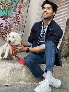 a man is sitting on the steps with his small white dog and wearing a red leash