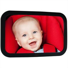 a baby in a red car seat smiling at the camera with his head turned to the side