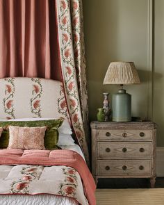 a bed sitting next to a dresser with a lamp on top of it