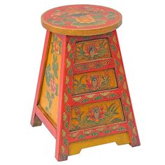 an orange and yellow painted wooden stool with floral designs on the top, sitting against a white background