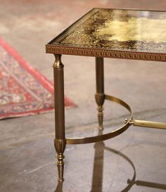 a small table with a glass top and gold trimmings on the legs, sitting in front of a rug