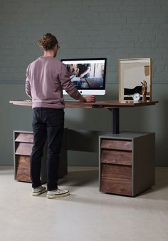 a man standing in front of a desk with a computer monitor on top of it