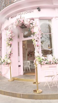 a pink store front with flowers on the windows and gold poles in front of it