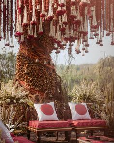 two red couches under a tree covered in flowers and hanging beads with white pillows