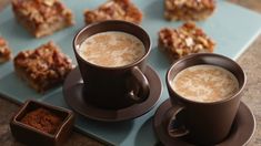 two cups of coffee sitting on top of a blue plate next to some desserts