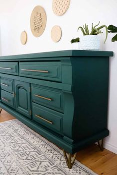 a green dresser with gold handles and brass pulls in a white living room, next to a potted plant