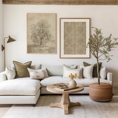 a living room with white couches and paintings on the wall above them, along with a coffee table