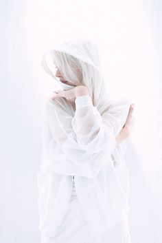 a woman with white hair is wrapped up in a white cloth and looking down at the ground