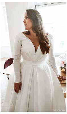 a woman standing in front of a window wearing a white dress and holding her hands on her hips