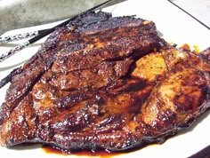 some meat is sitting on a plate next to utensils and a knife in front of it