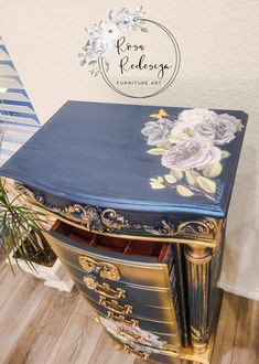 an ornate blue and gold chest with flowers painted on the front, sitting next to a potted plant