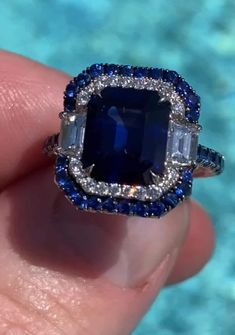 a close up of a person's hand holding a blue and white diamond ring